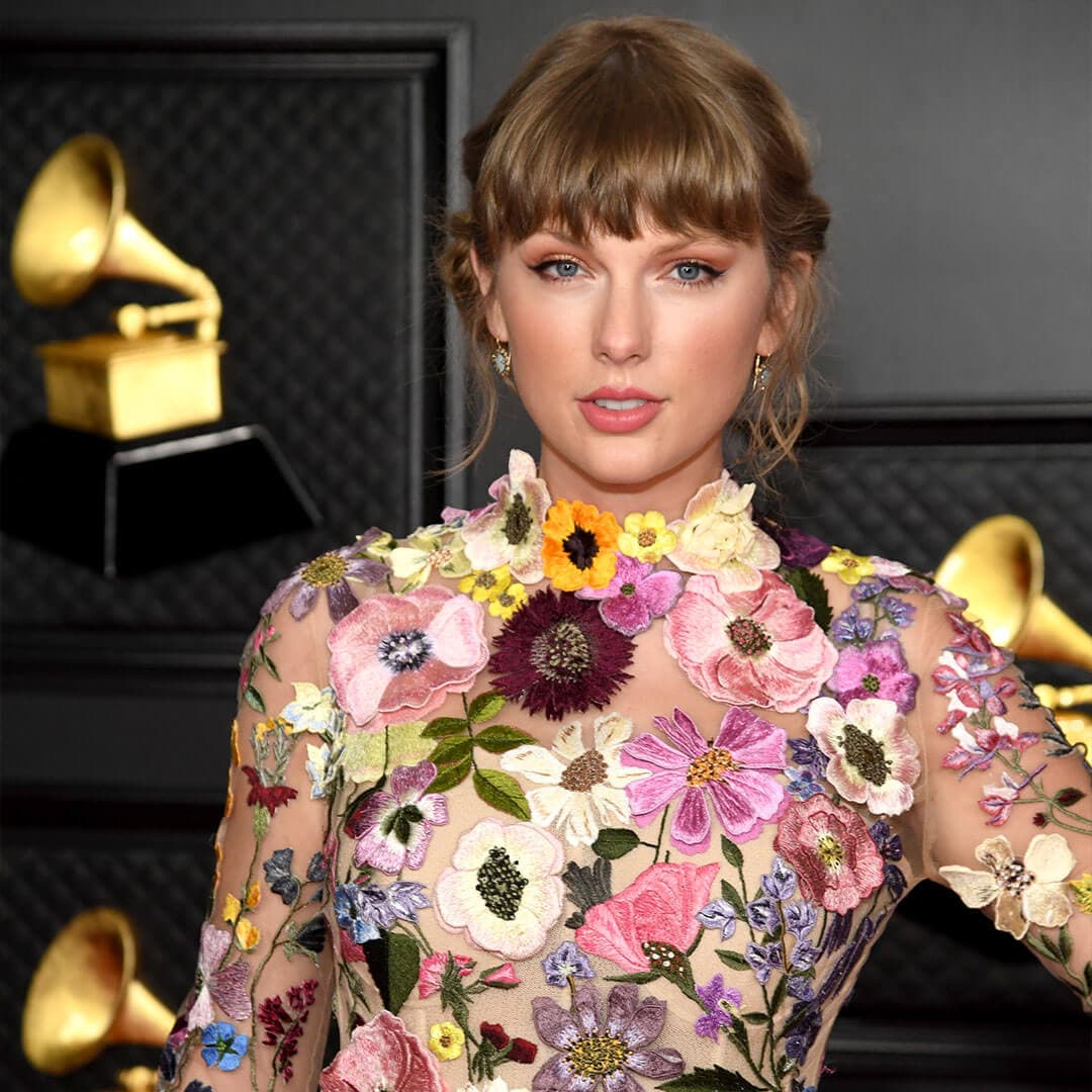 An image of Taylor Swift showcasing a soft monochrome look, with coral lipstick that complements her eyeshadow, wearing a sheer mesh dress embellished with flowers