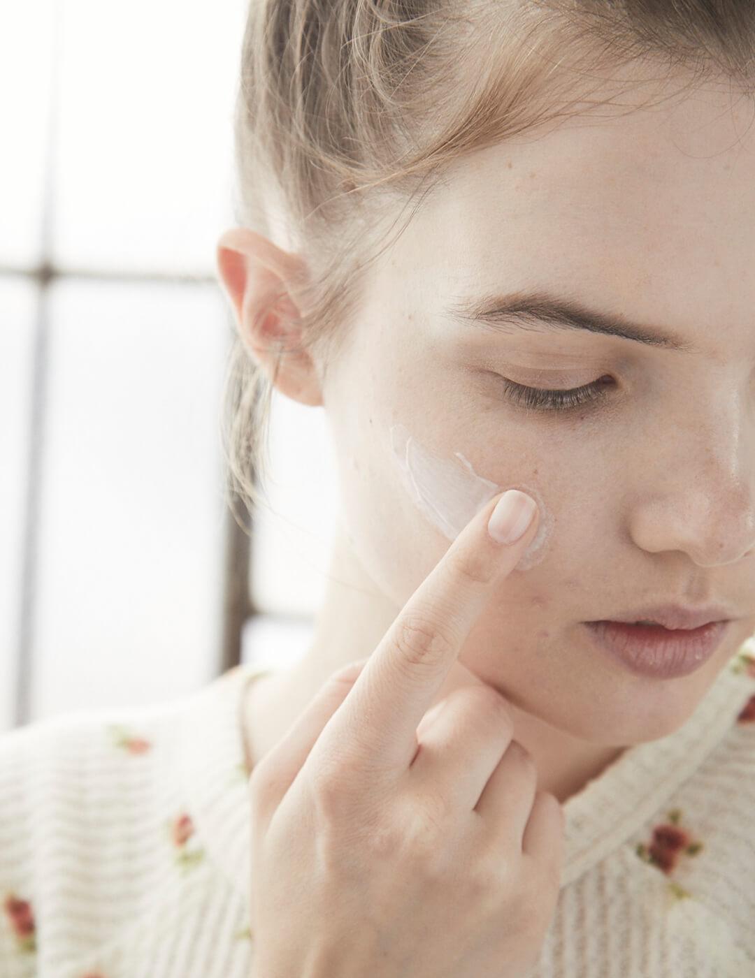 A close-up image of a model applying cream on her cheek