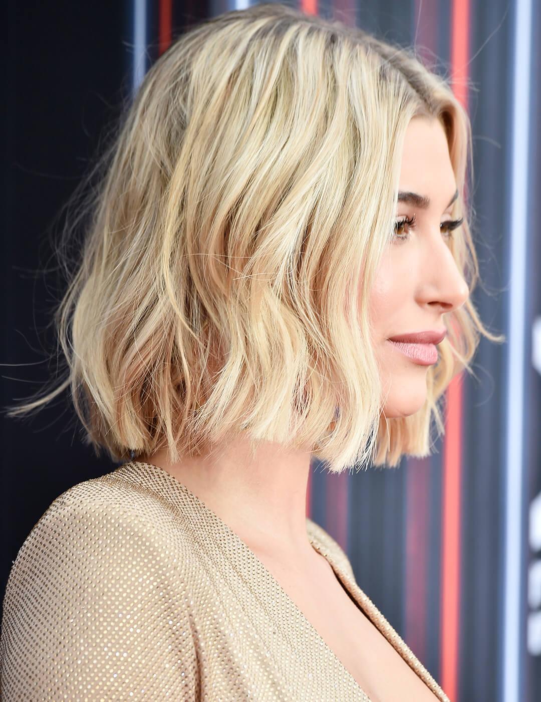 A photo of Hailey Baldwin in sideways characterized by her messy, long bob blonde hair dressed in a stunning beige gown on an abstract background