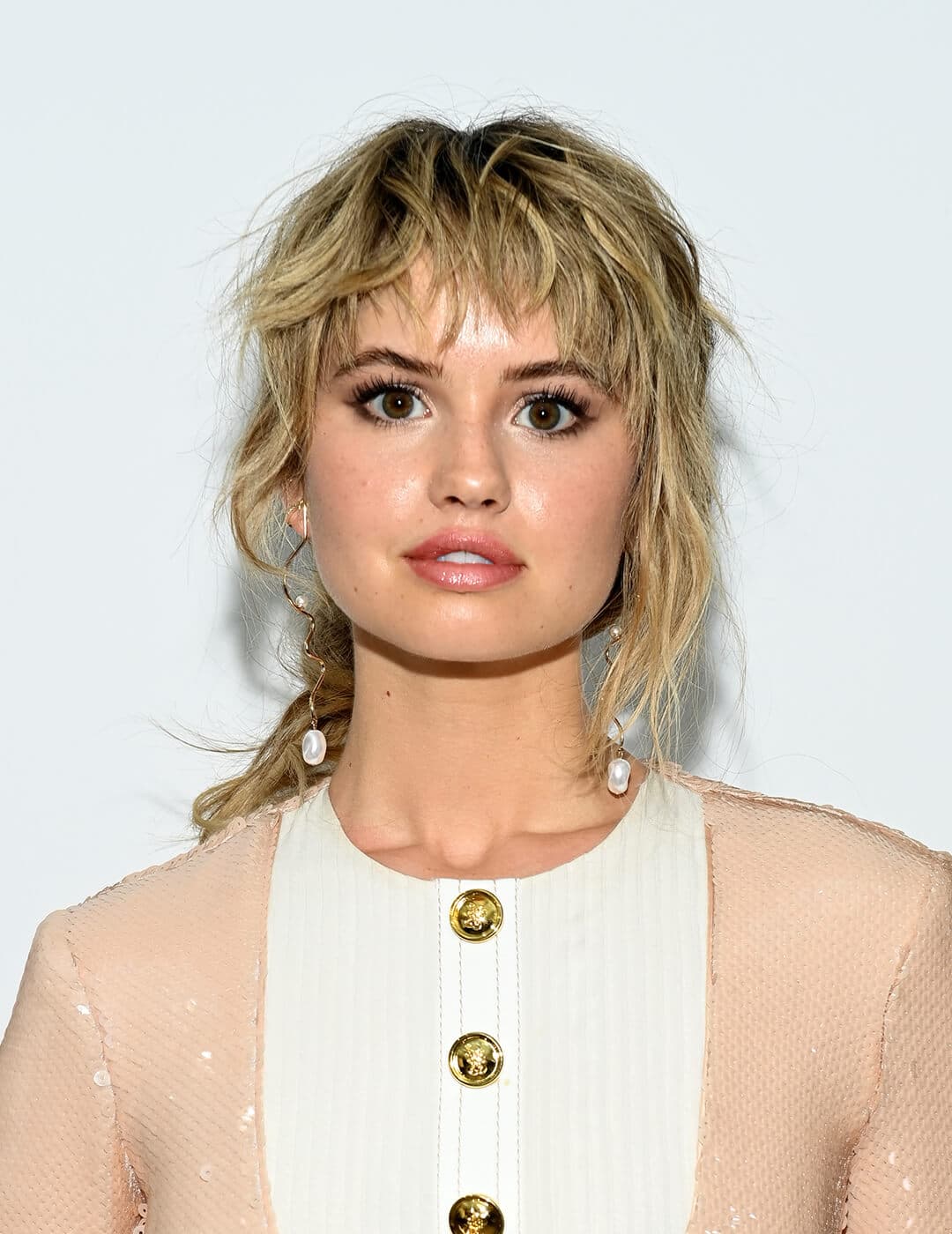 An image of Debby Ryan sporting her shag-meets-mullet hairstyle wearing a peach long sleeve dress with gold buttons  