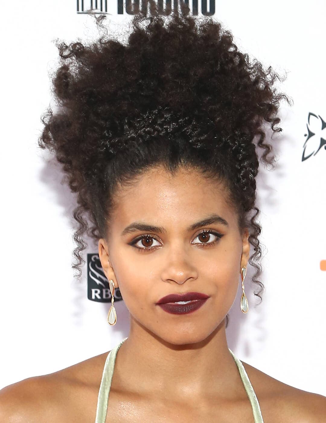 Zazie Beetz in a spaghetti strapped dress and rocking a curly updo with braided hair as headband