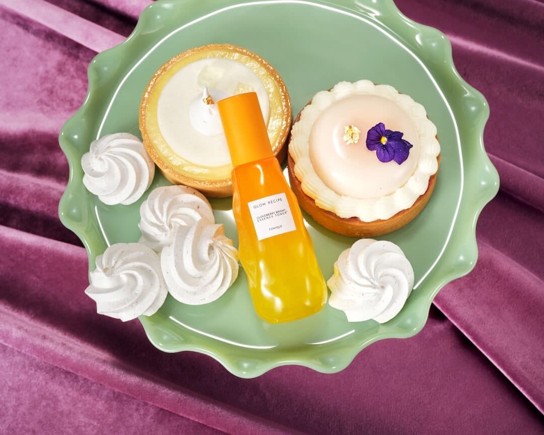 GLOW RECIPE Cloudberry Bright Essence Toner on a mint green dessert plate surrounded by tea desserts