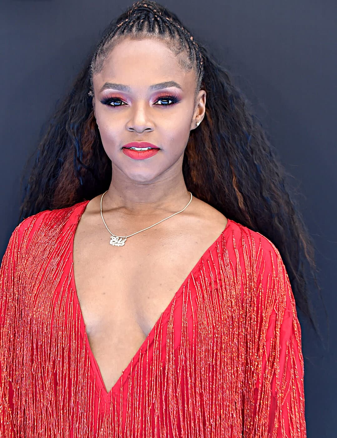 Gia Peppers rocking cornrows with half ponytail hairstyle, red monochromatic makeup look and red fringe dress