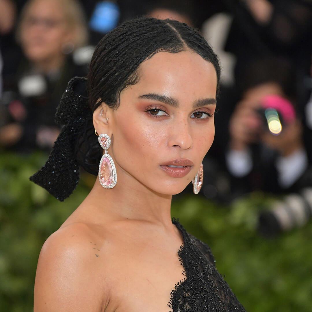 An image of Zoe Kravitz, with her Warm Neutral Monochromatic Makeup wearing a black mesh dress and her huge pink teardrop shape diamond earing
