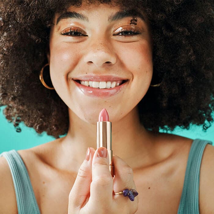 A woman with curly hair and a bright smile, showcasing a pink lipstick shade suitable for her skin tone