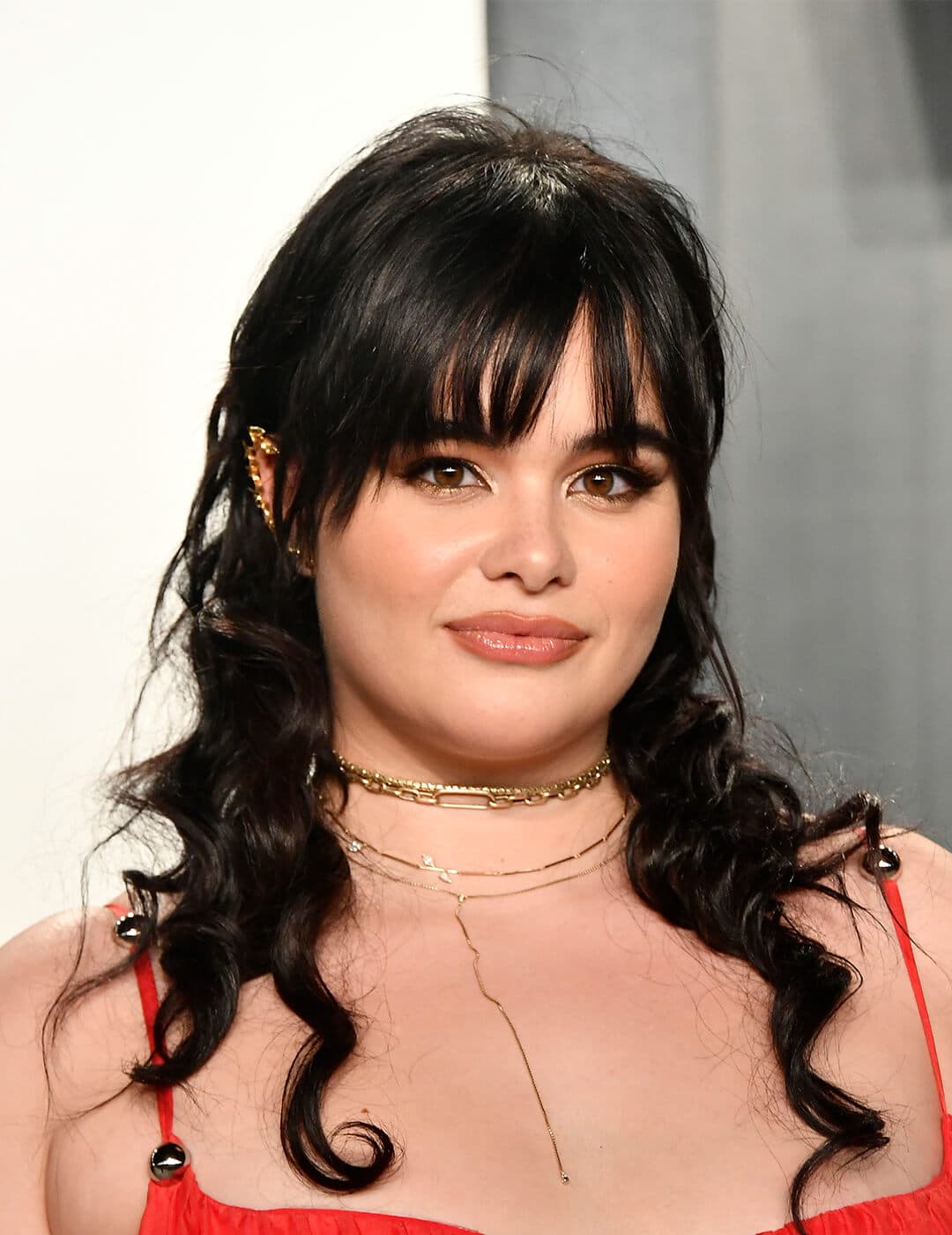 An image of Barbie Ferreira with a dark wavy mullet in a red dress wearing a golden necklace