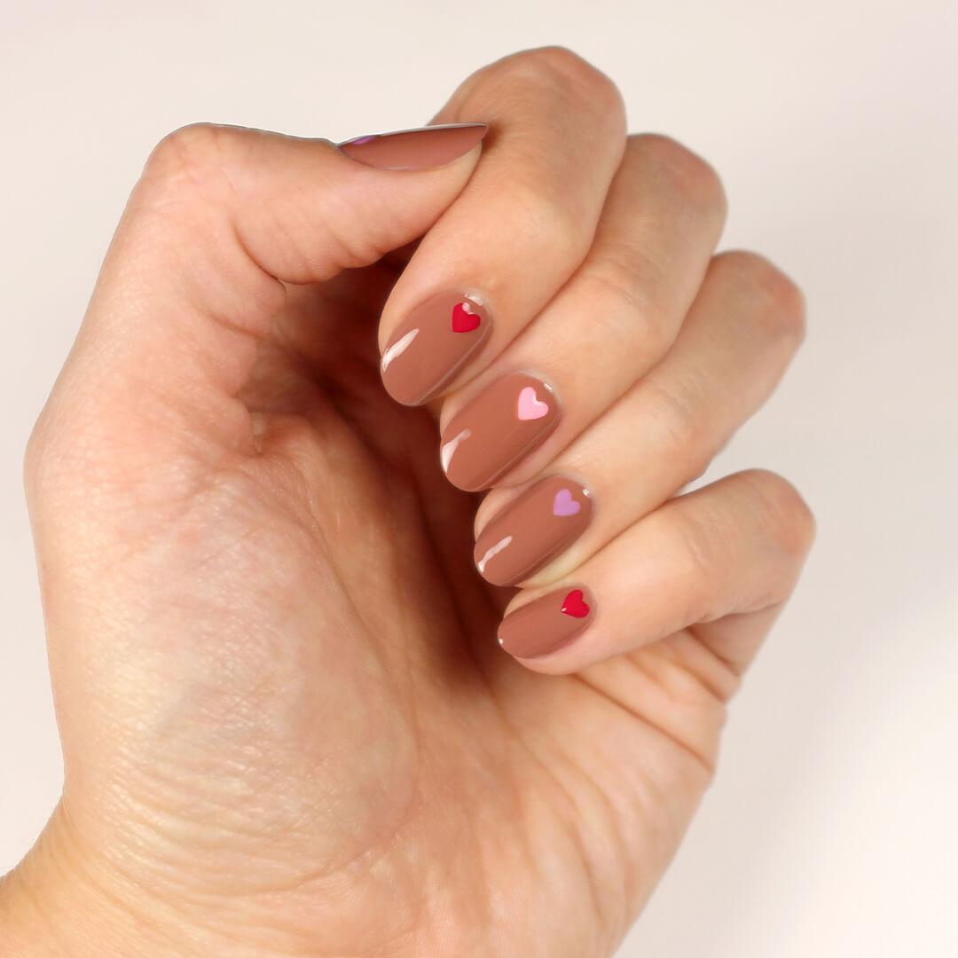 Close-up of a model's hand with nude nail polish with pink, red, and purple hearts nail art