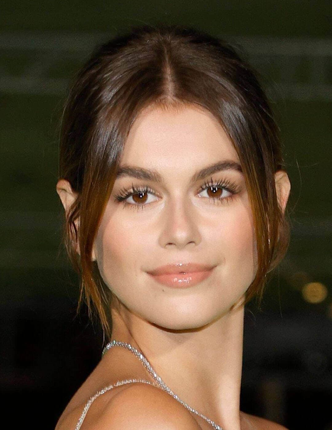 A photo of Kaia Gerber in her charming smile using a nude-colored lipstick in her updo hairstyle with two side bangs