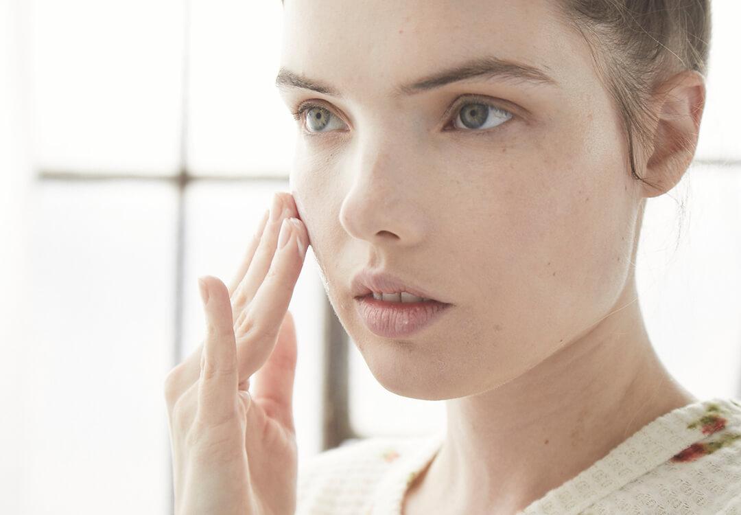 An image of a model applying cream on her cheek