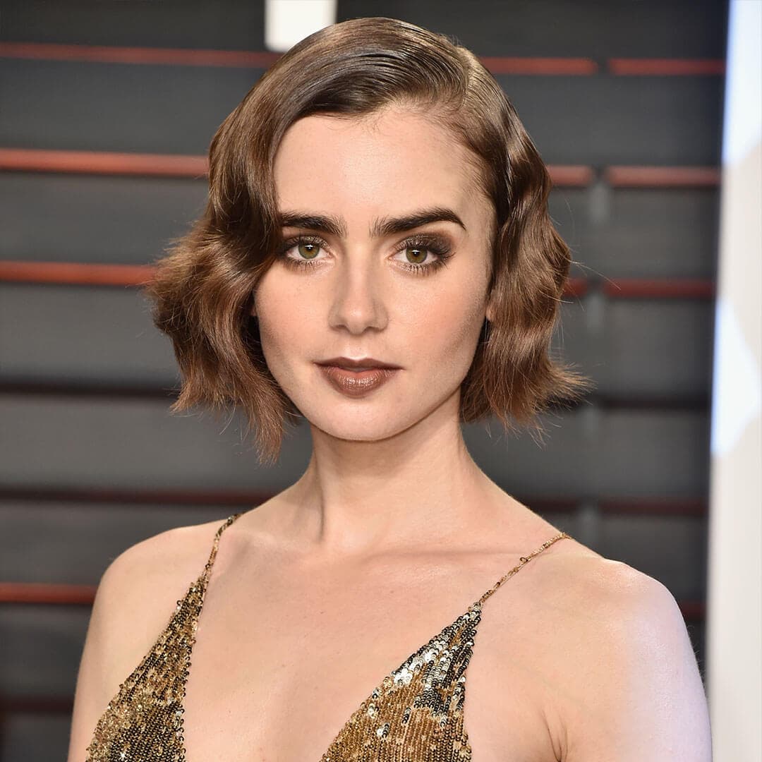 An image of Lily Collins, with her Retro Glam Monochromatic Makeup wearing a gold sequined plunge halter top dress staring straight at the camera