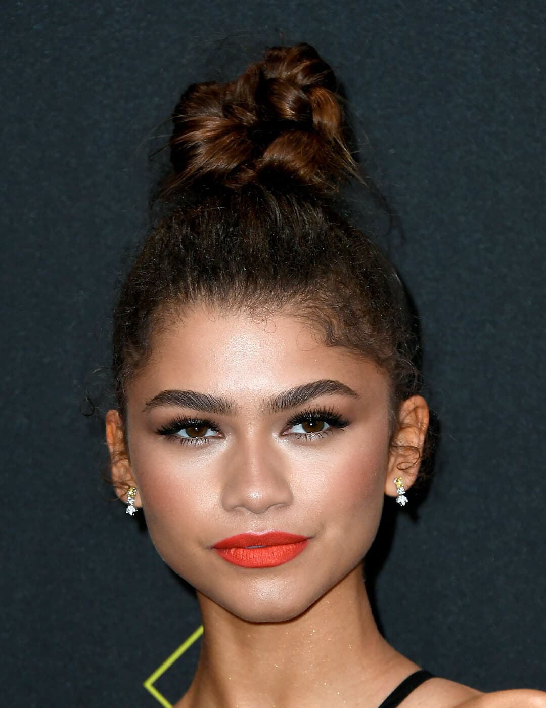 Zendaya looking glam in a top knot hairstyle paired with a bold coral lipstick