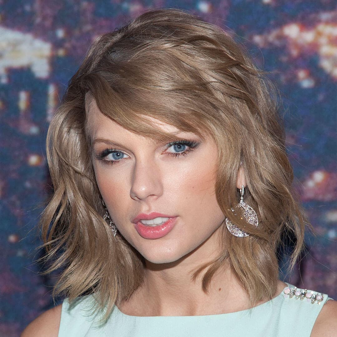 An image of Taylor Swift with her short, wavy hair and minimal makeup that includes teal eyeshadow and peachy lipstick, clad in a teal top