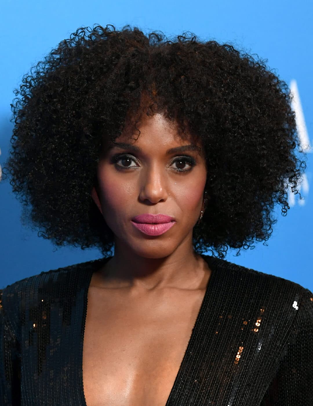 Close-up of Kerry Washington in a black sequined dress rocking an afro against blue background