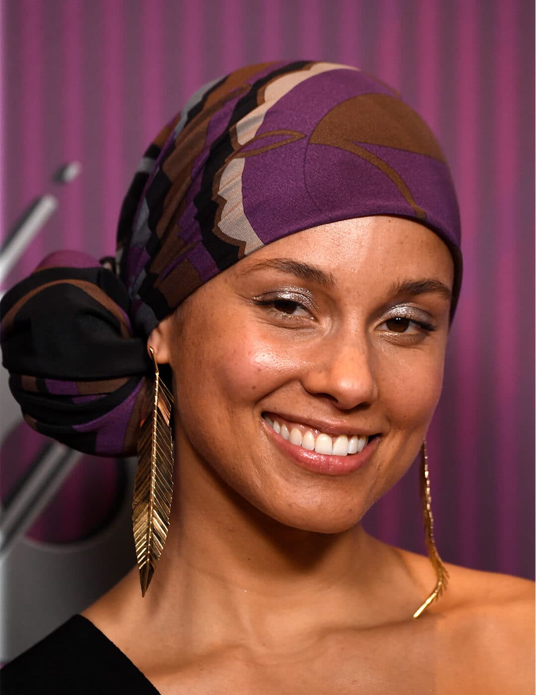 Close-up of a smiling Alicia Keys rocking a headwrap and danging, gold feather earrings