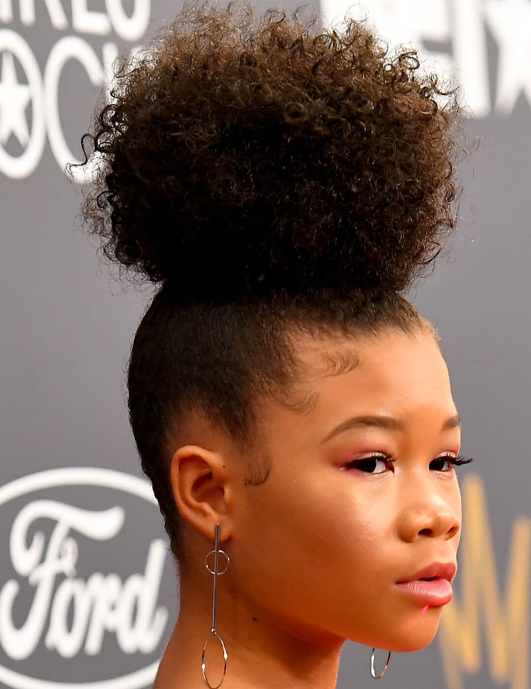 Storm Reid sporting a curly updo hairstyle and gold dangling earrings