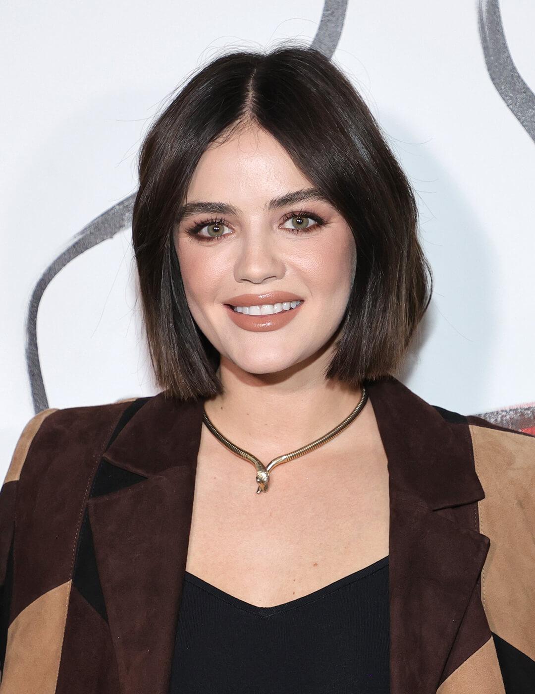 A photo of Stacey Bendet wrapped in a neutral colored coat and flashes her charming smile using a nude lipstick that compliments her dark brown bob cut hair