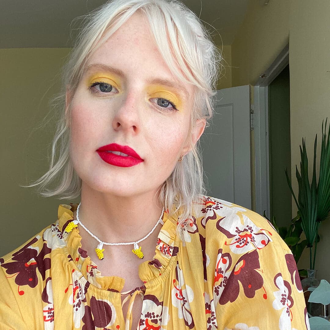 Close-up image of Hannah Cassidy rocking a bold yellow eyeshadow and bold red lipstick look in a yellow floral outfit