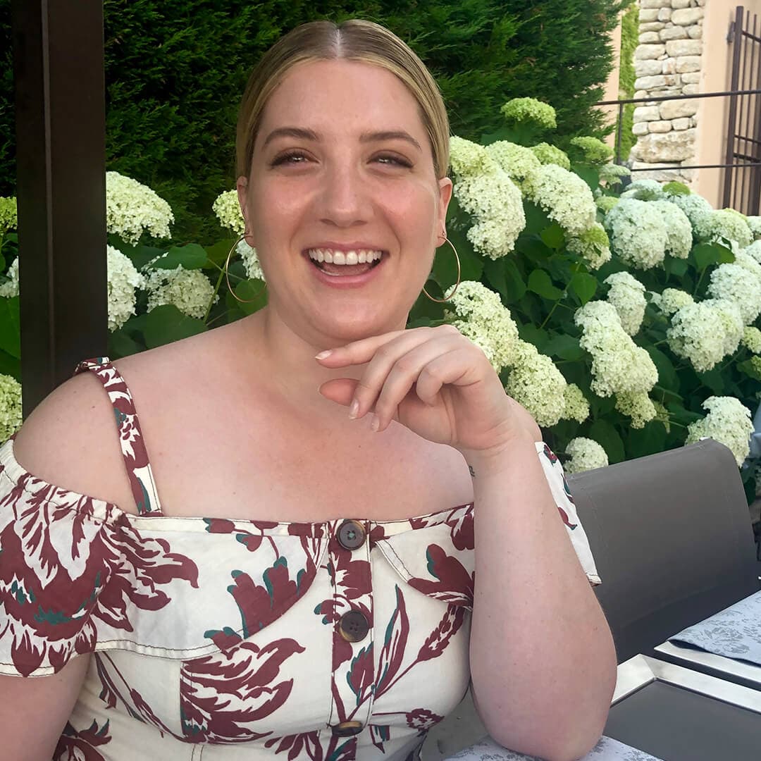 Close-up image of Maddie Aberman smiling while posing with white flowers in the background