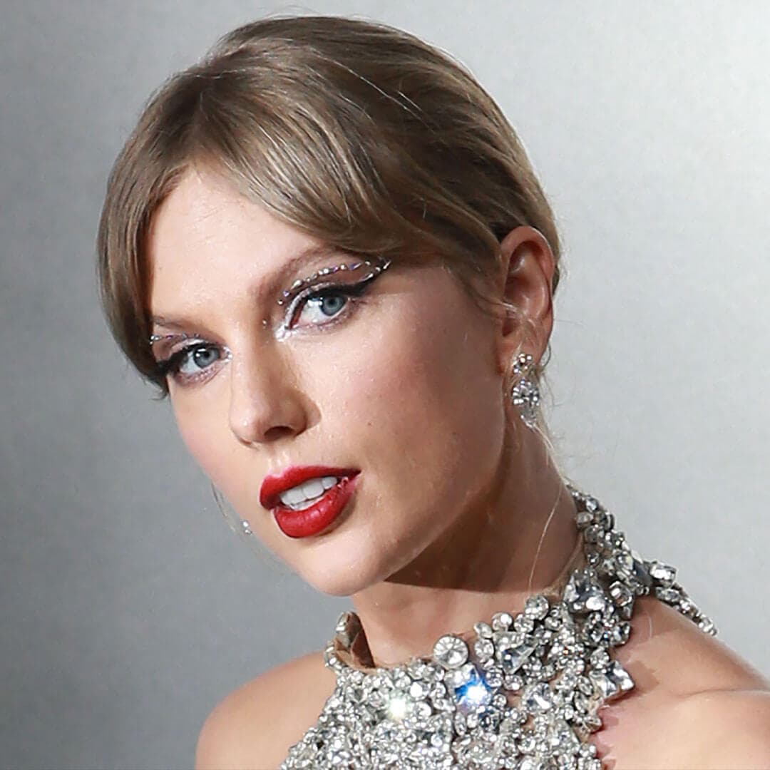 An image of Taylor Swift wearing a Bejeweled Sparkles see-through dress sheer dress made of nude mesh, featuring her bangs styled in a split and complemented by a striking red lipstick