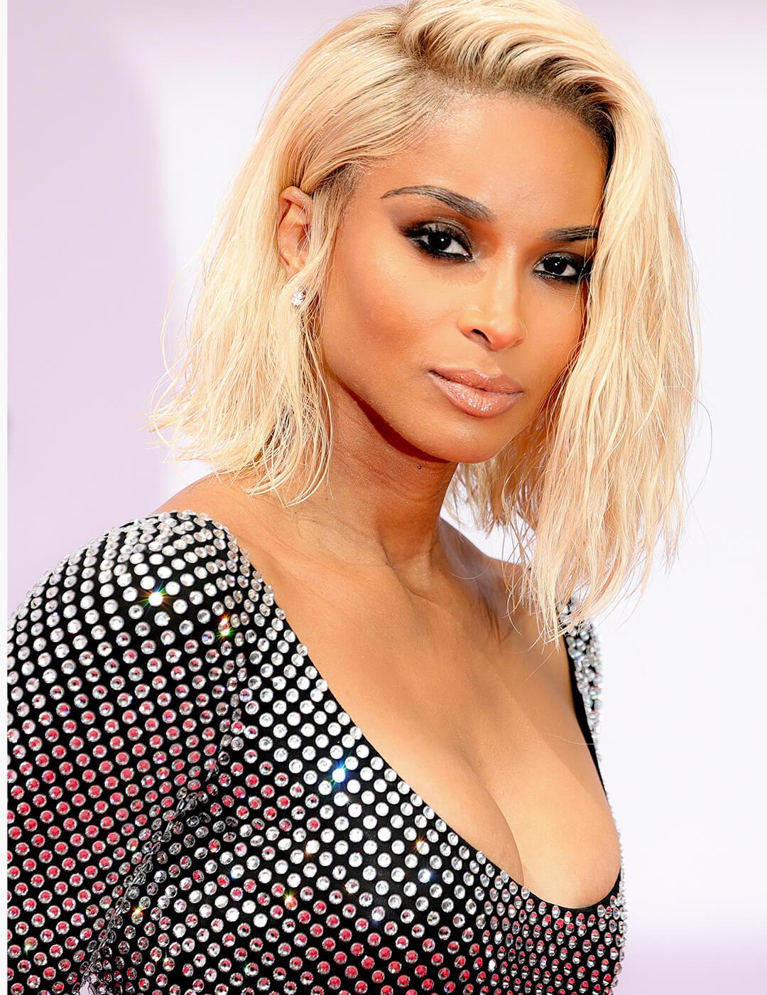 A photo of Ciara wearing a dazzling low cut dress in her mid-length blond hair tucked in her ear