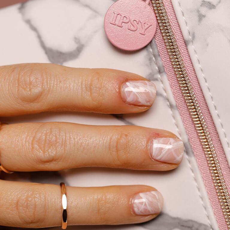 An image of three fingers with pink and white marble nail art resting on a pink and grey marble designed bag