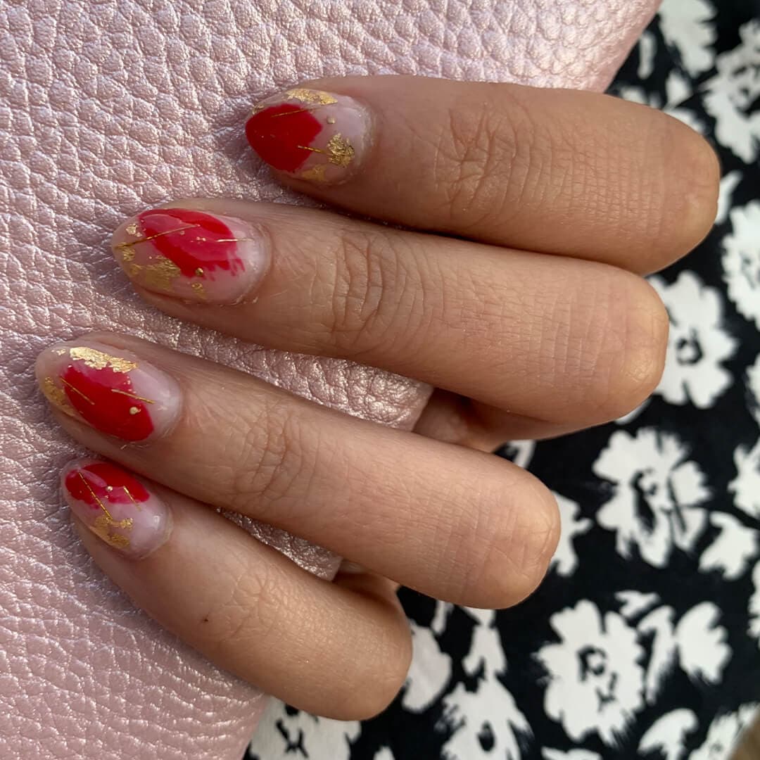 Image of a hand with red and gold abstract nail art holding a rose gold pouch