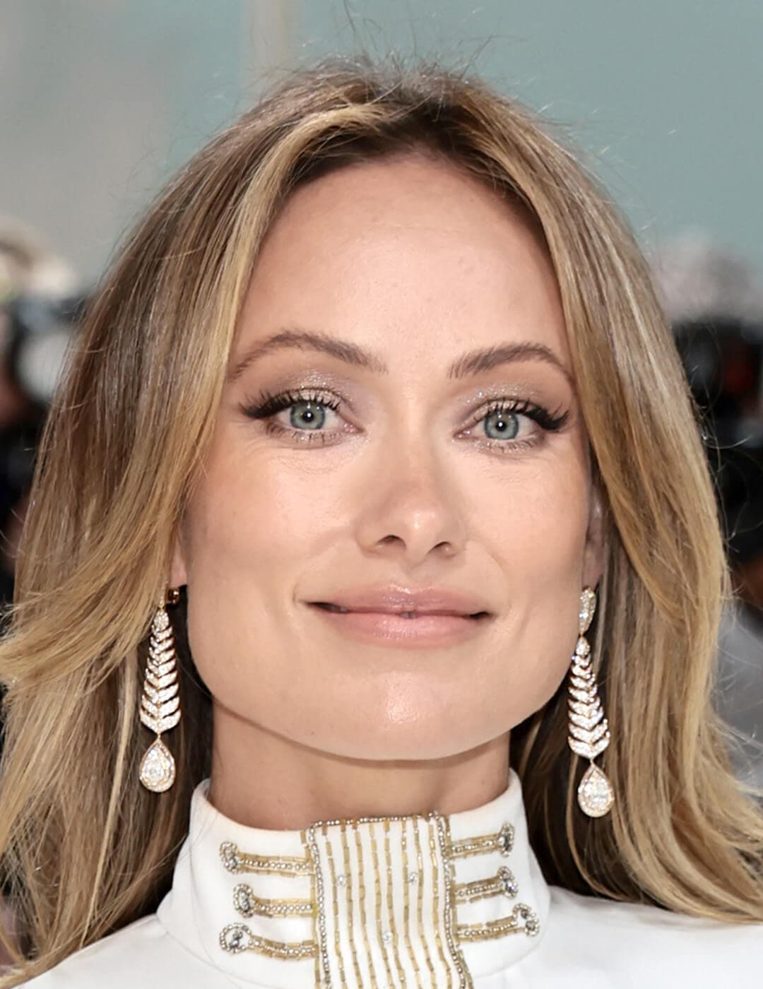 Close-up look of Olivia Wilde sporting a subtle makeup look, her blonde locks framing her face, and accessorizing with drop earrings, all while rocking a stunning white gown