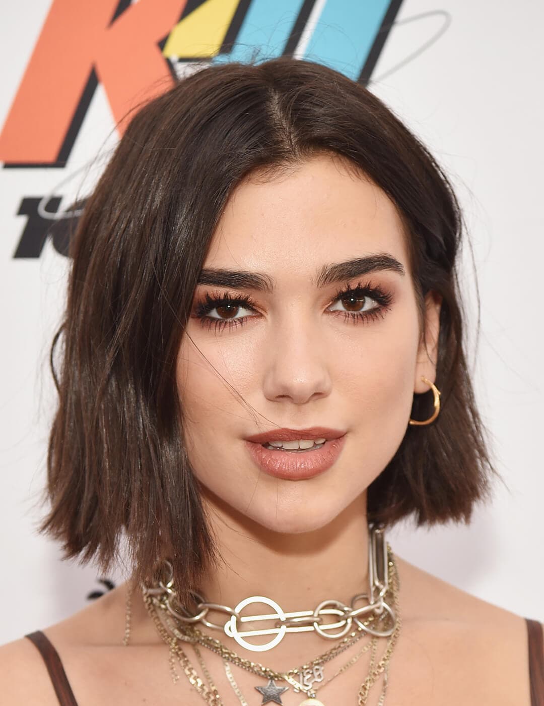 An image of Dua Lipa looking fierce and fresh in her brown semi-smokey eyeliner and lipstick along with chained necklace 