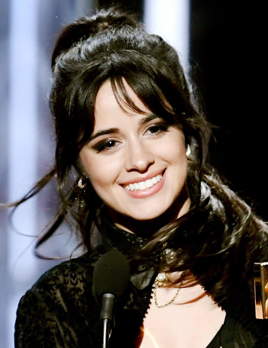 Camila Cabello smiling in an all-black ensemble and dark smoky eye makeup look