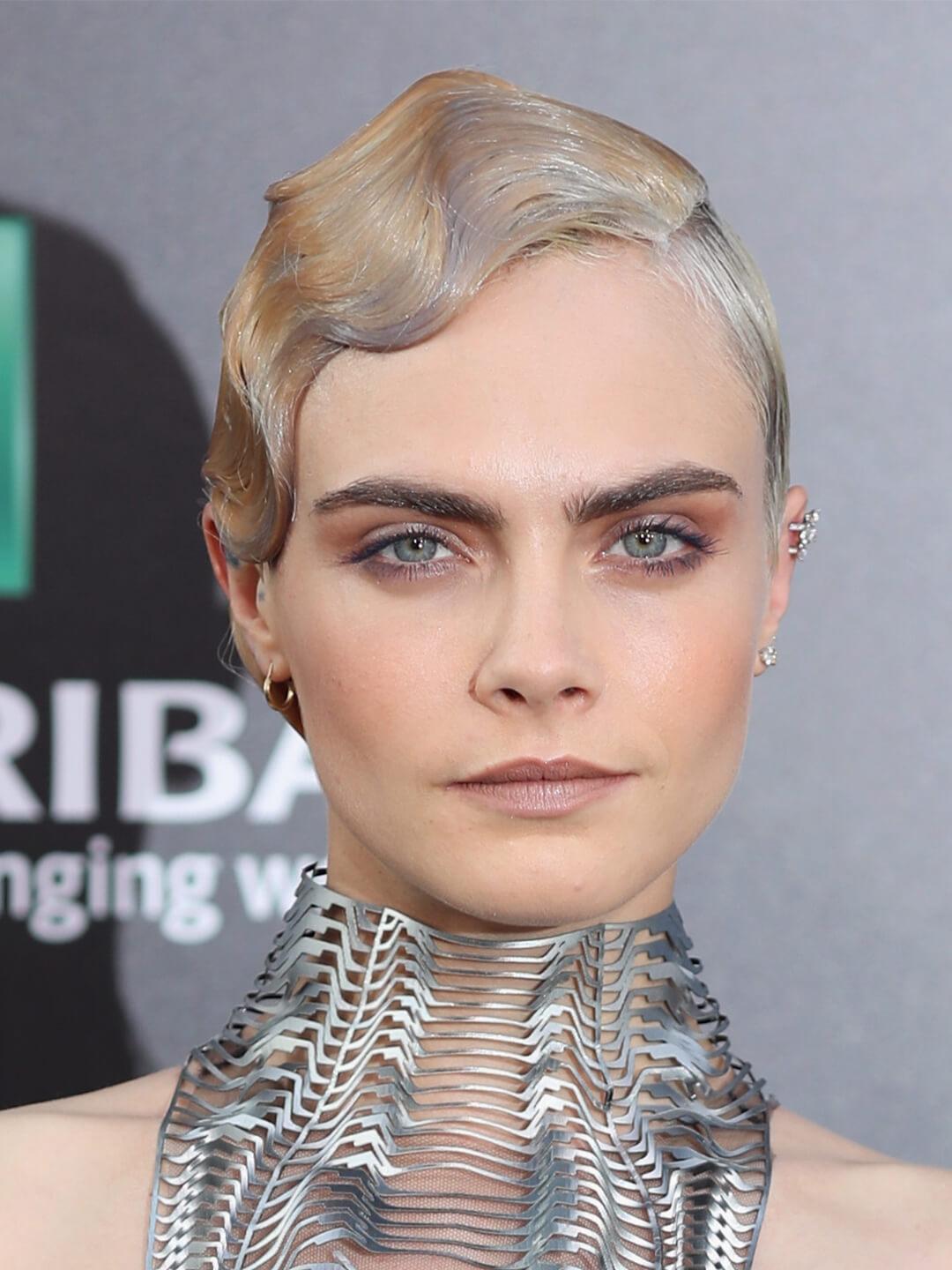 Cara Delevingne rocking a sleek and wavy short hairstyle and futuristic neck piece