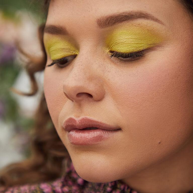 A close-up image of a model wearing neon lime green eyeshadow looking down