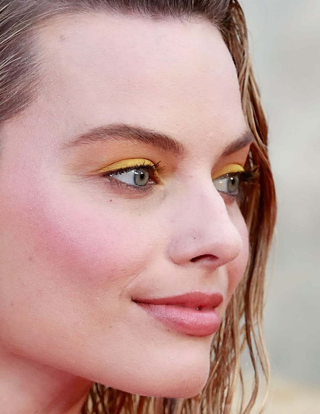 Close-up side profile image of Margot Robbie rocking a bright yellow eyeshadow makeup look