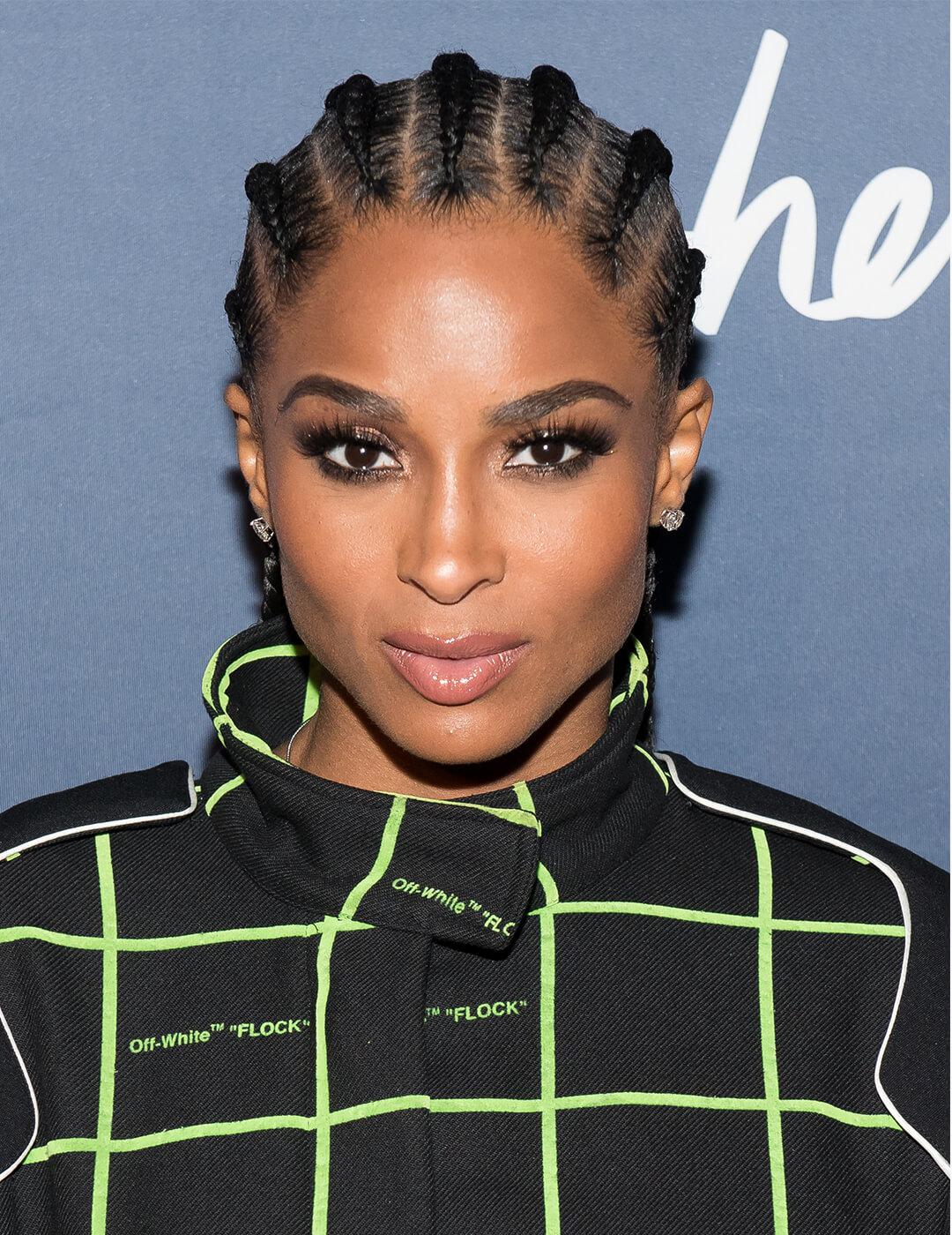 Close-up of Ciara rocking a cornrows hairstyle, smoky eye eyeshadow makeup paired with nude lips, and a black jacket with neon green intercrossing lines