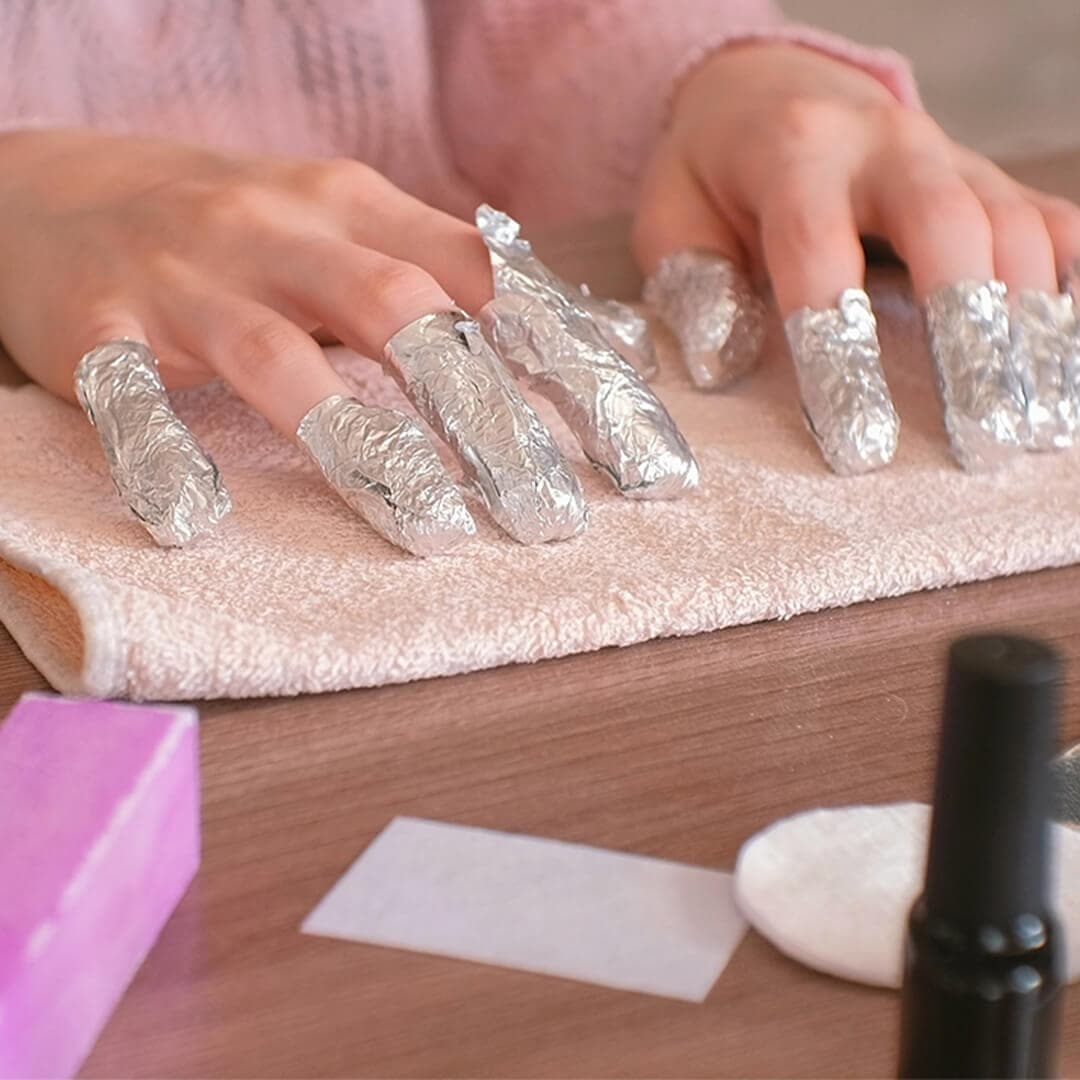 Close-up image of woman's fingers each wrapped in tin foil resting on a small towel