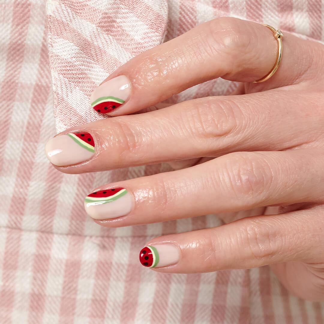 Close-up image of a hand with watermelon nail art mani against a checkered pink and white background