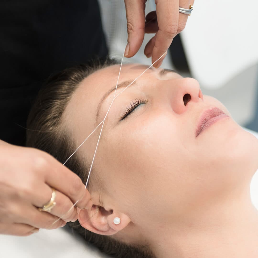 Image of a woman's hands threading another woman's eyebrow
