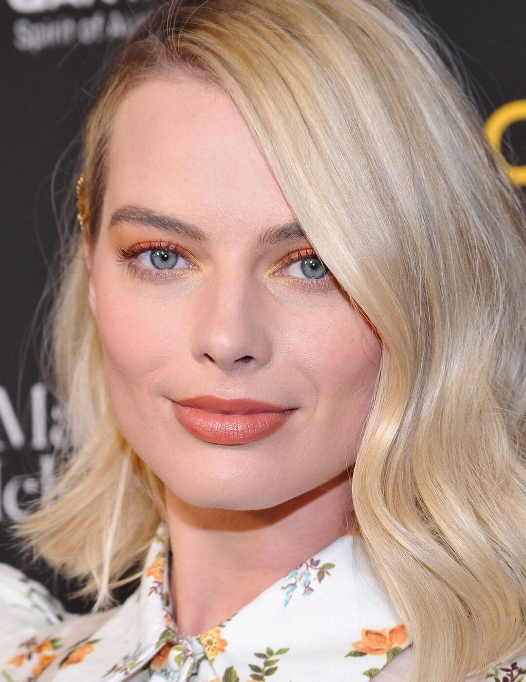 A photo of Margot Robbie wearing a floral dress and an orange eyeshadow