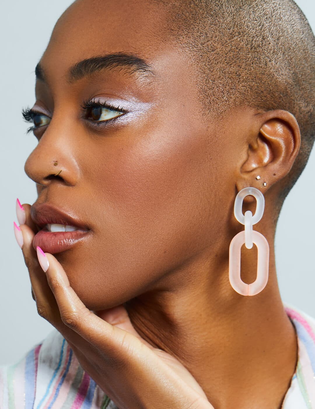Side profile of a beautiful Black woman rocking a silver eyeshadow makeup look and frosty chains earrings