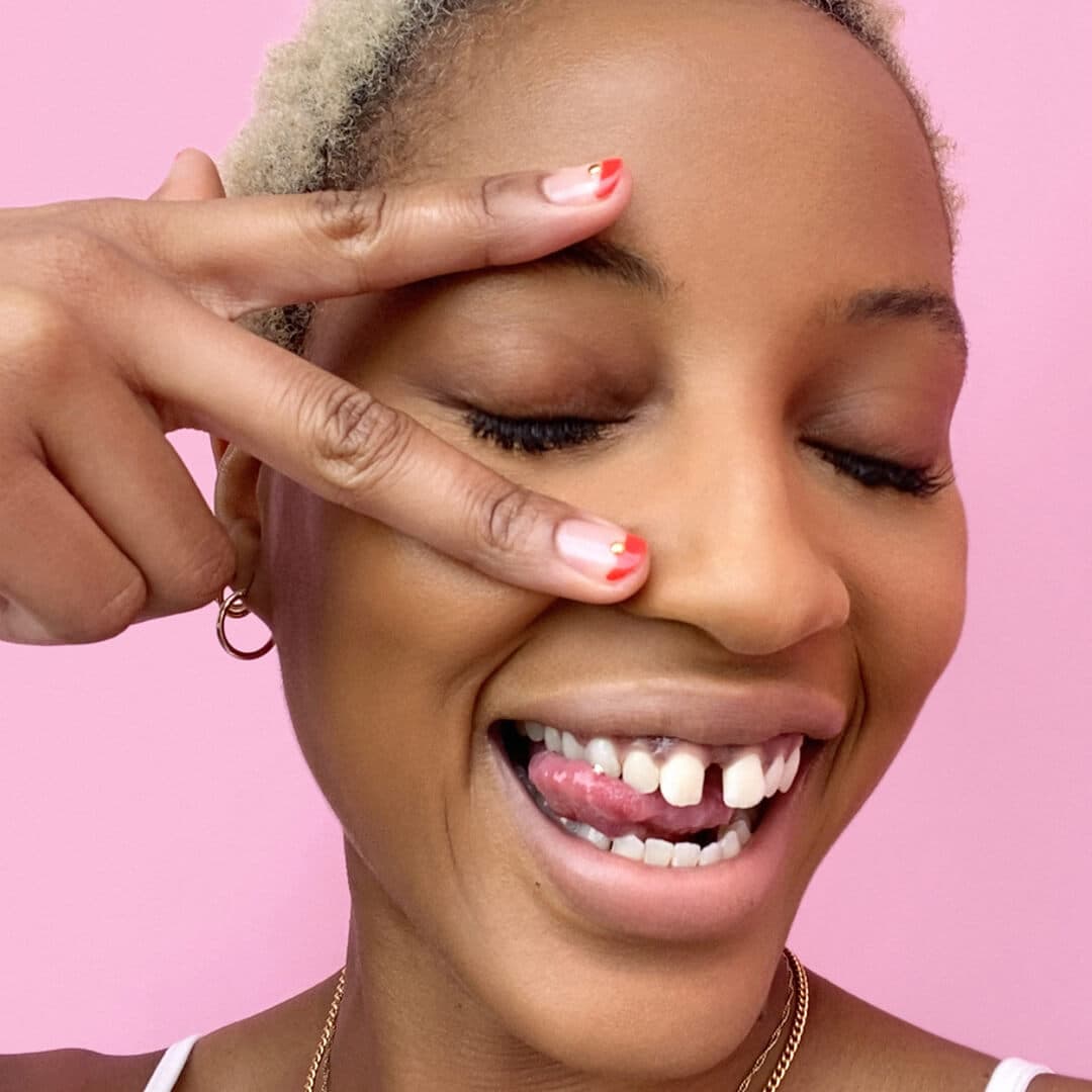 Close-up of a Black model making a wacky face and showing her red and gold nail art