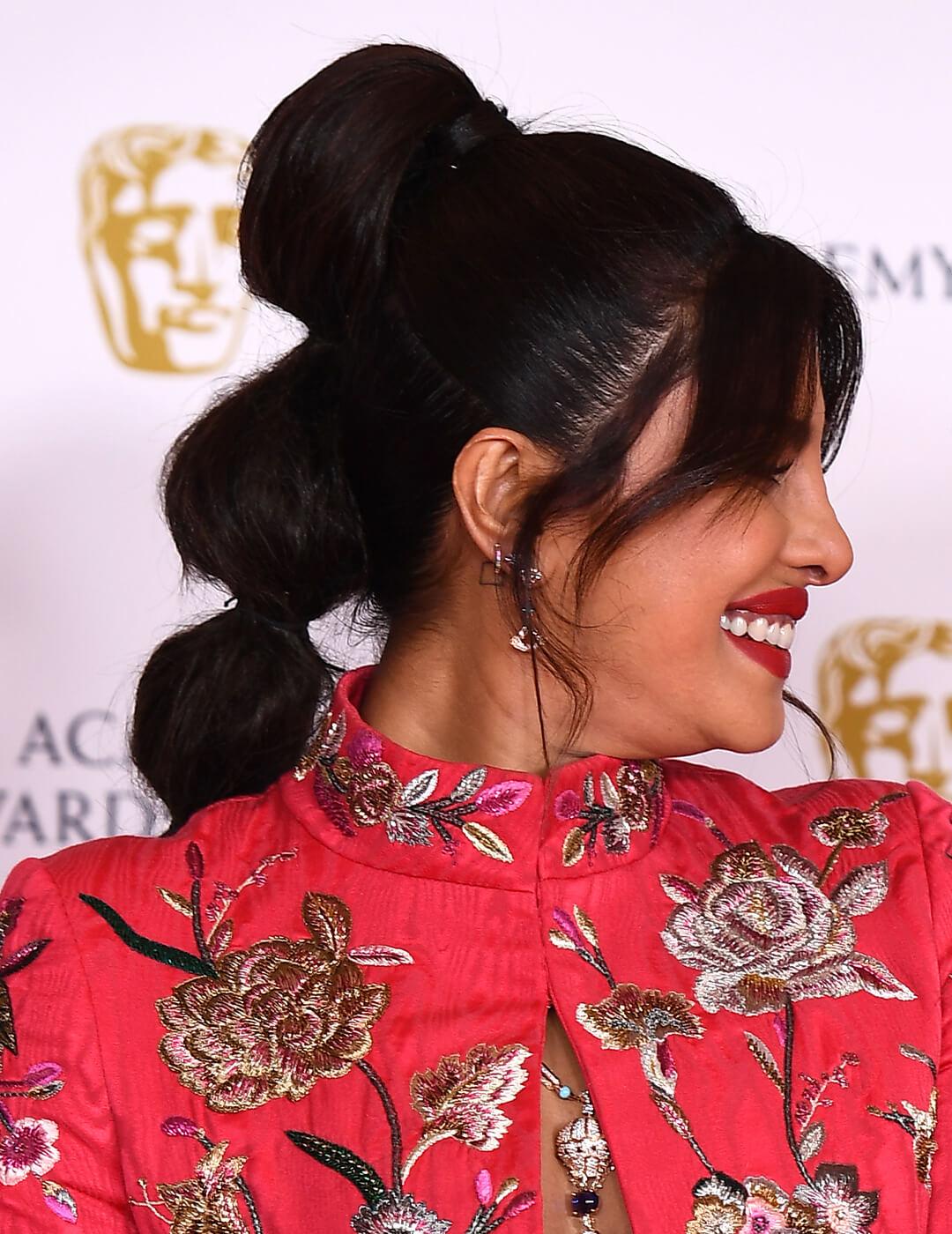 Close-up side profile of Priyanka Chopra Jonas rocking a bubble ponytail hairstyle and red floral dress