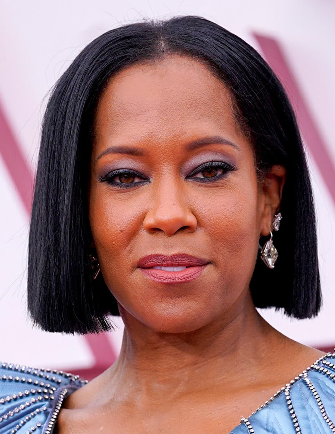 A photo of Regina King showcasing her straight, black bob haircut on a pink background