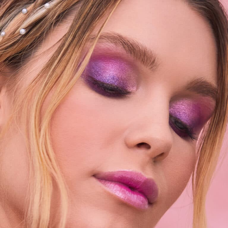 A closeup image of a model wearing pink to purple gradient eyeshadow paired with a pink lip gloss