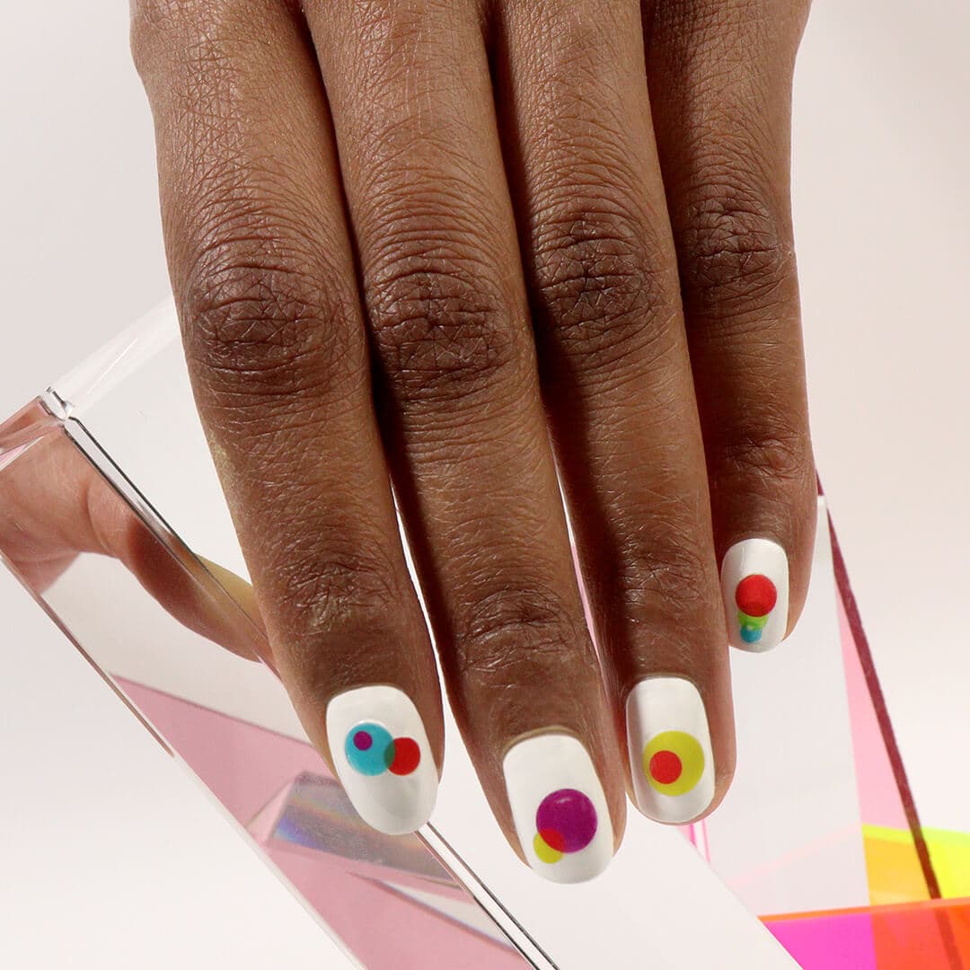 A closeup of a hand with white base nail polish and colorful nail decals