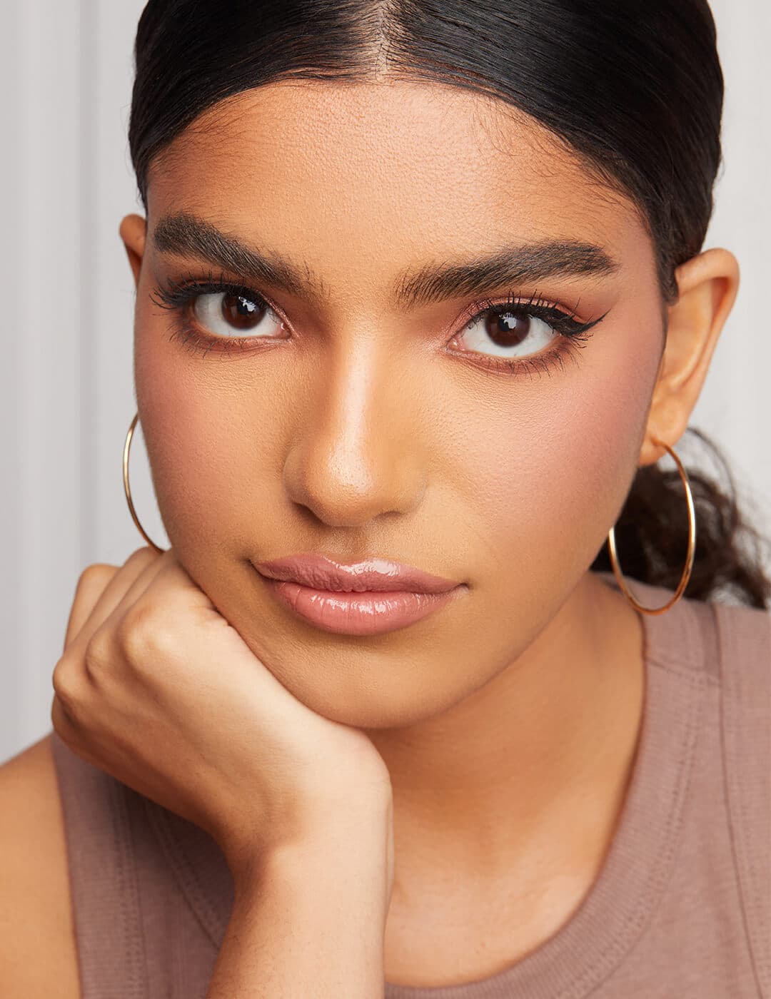 Close-up of a model with rose gold eyeshadow makeup look, nude pink lips, and gold hoop earrings