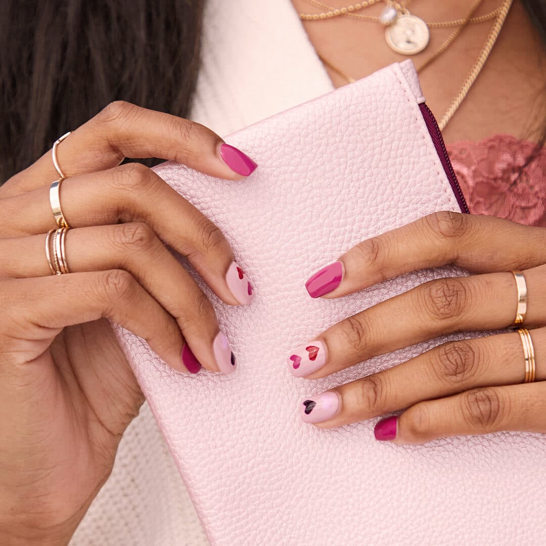 Image of model's hands with pink hearts nail art holding a pink pouch