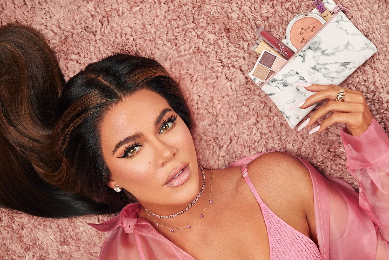 Khloé Kardashian holding an IPSY January 2020 Glam Bag while lying on pink carpet