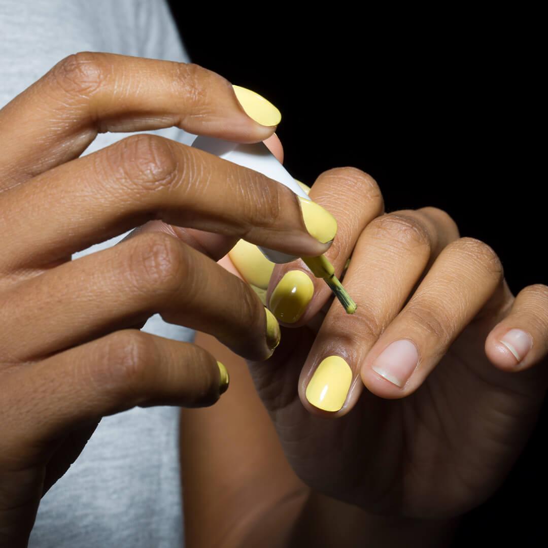 Close-up of woman's hands applying pastel yellow nail polish