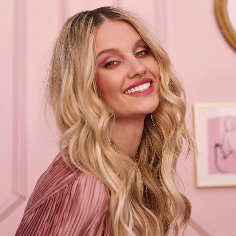 An image of a smiling model with blonde, loose wavy hair