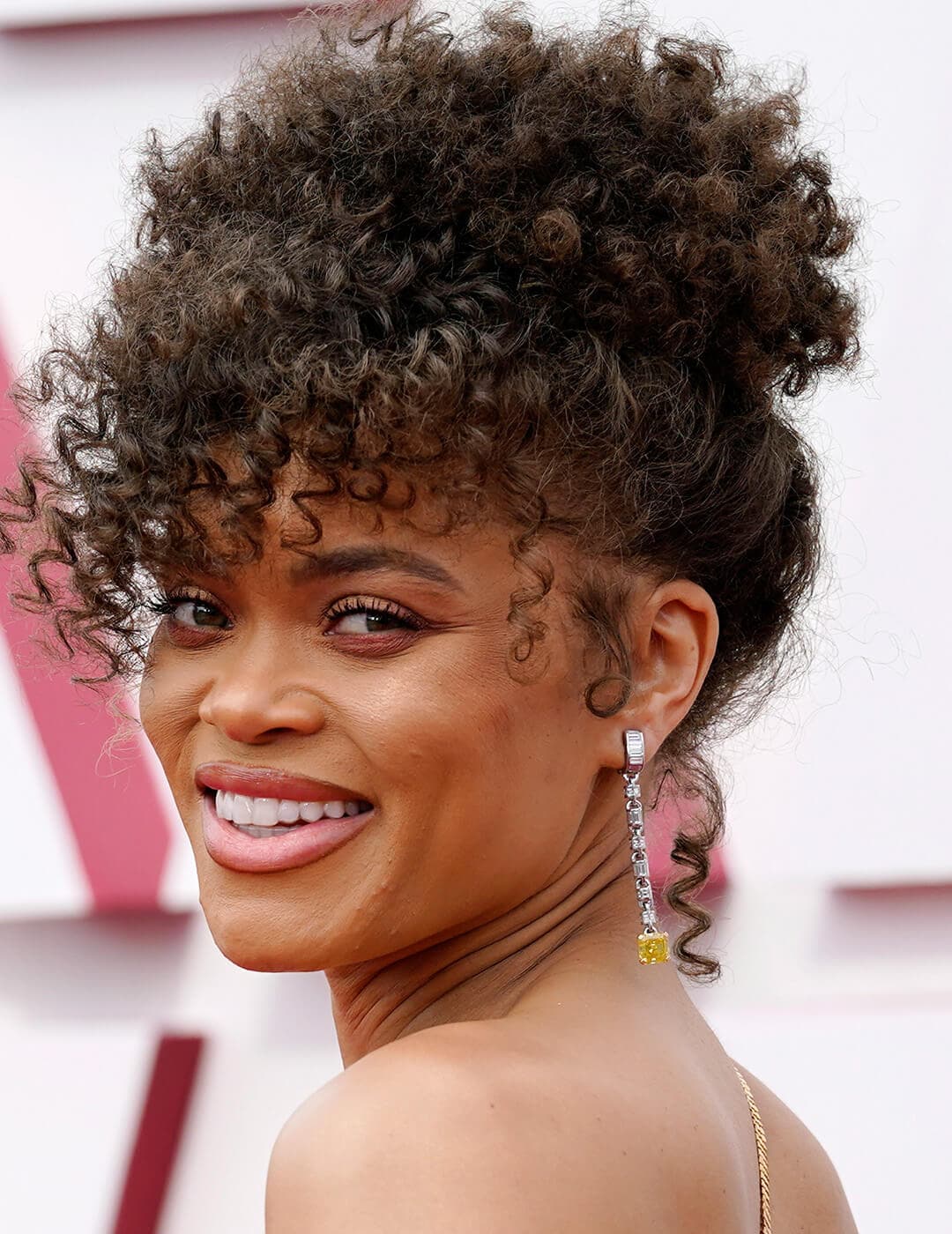 An image of Andra Day wearing a long yellow-end silver earring with a french-twist hairstyle