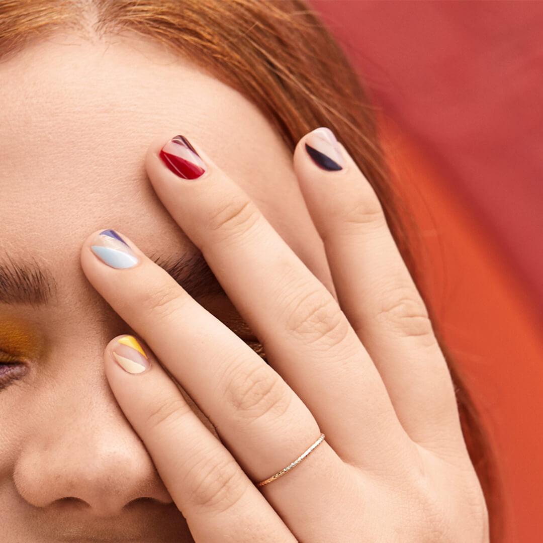 Image of a model's hand with multicolored negative space stripe nail art against her face